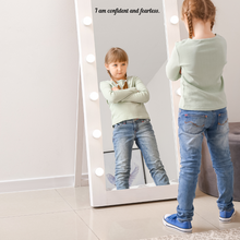 Load image into Gallery viewer, A young girl with braids stands confidently before an illuminated mirror, arms crossed. Reflection shows strong expression. A decal on the mirror above reads "I am confident and fearless."