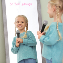 Load image into Gallery viewer, A smiling child with braided hair holds a microphone, gazing at her reflection in a mirror. A decal on the mirror "Be You, Always" is written above her in pink.
