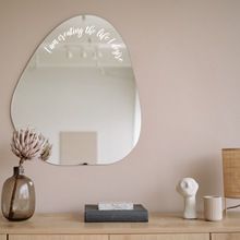 Load image into Gallery viewer, Organic-shaped mirror with the text "I am creating the life I desire" reflects a minimalist room. Below, a vase with a dried flower and decor add a calming touch.