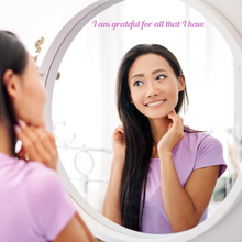 Load image into Gallery viewer, Woman in a lavender shirt smiling at her reflection in a round mirror with the text "I am grateful for all that I have" above her, conveying positivity.