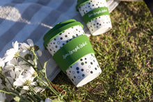Load image into Gallery viewer, A green-dotted reusable cup with "Live Laugh Label" on a picnic blanket next to white daisies on sunlit grass, evoking a cheerful, serene picnic vibe.