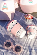 Load image into Gallery viewer, Two pink polka dot keep cups, pastel caps with letters, a pink cupcake, and flower-shaped sunglasses on a purple checkered cloth in sunlight.