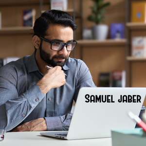 Picture of a man at a work desk with a laptop with a decal that says Samuel Jaber in black font